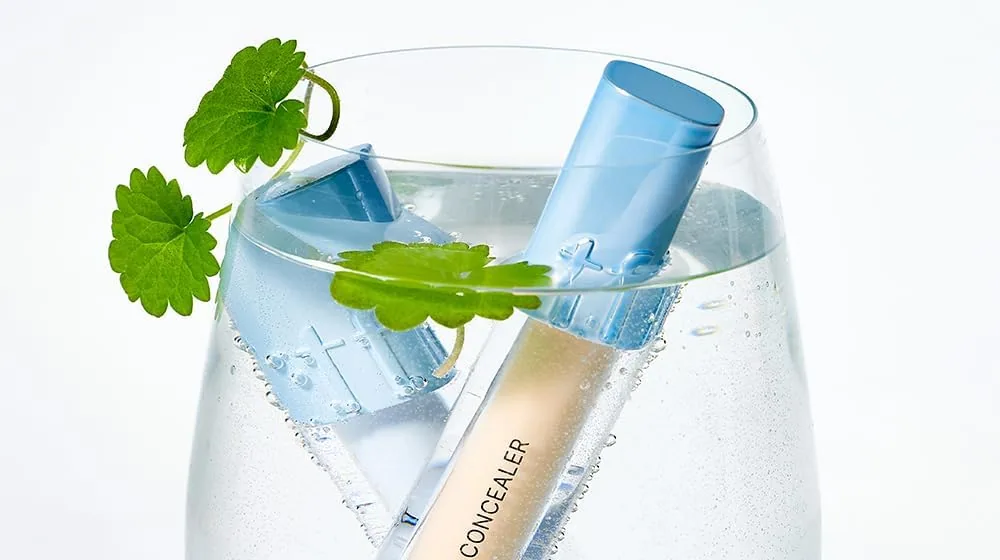 A TFIT Idol Cover Concealer tube in a glass of water with green leaves