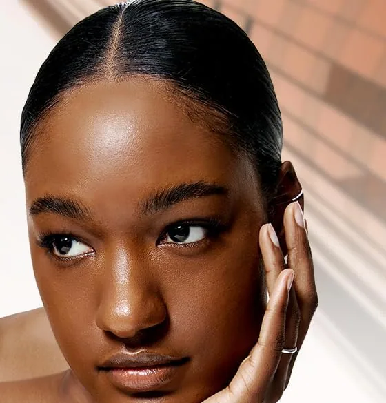 A model with deep skin resting her cheek on her hand, wearing TFIT Sleek Fit Cover Foundation